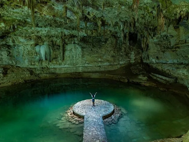 Une personne debout, les bras levés, sur la plateforme circulaire du Cenote Suytun.