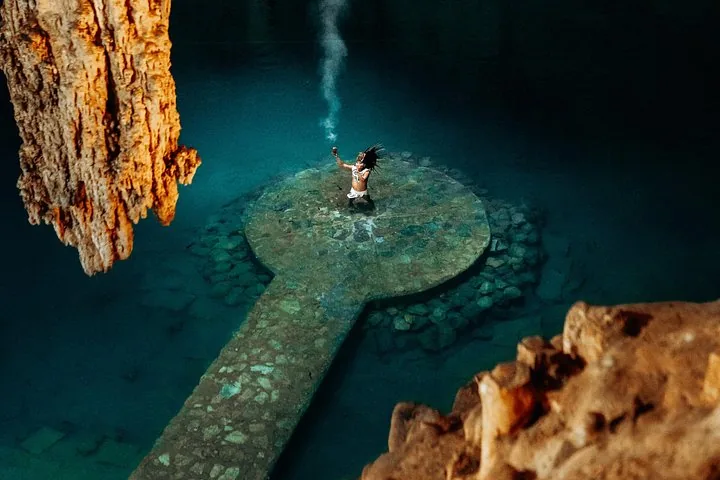 Une personne se tient sur la plateforme en pierre du Cenote Suytun, tenant un objet fumant.