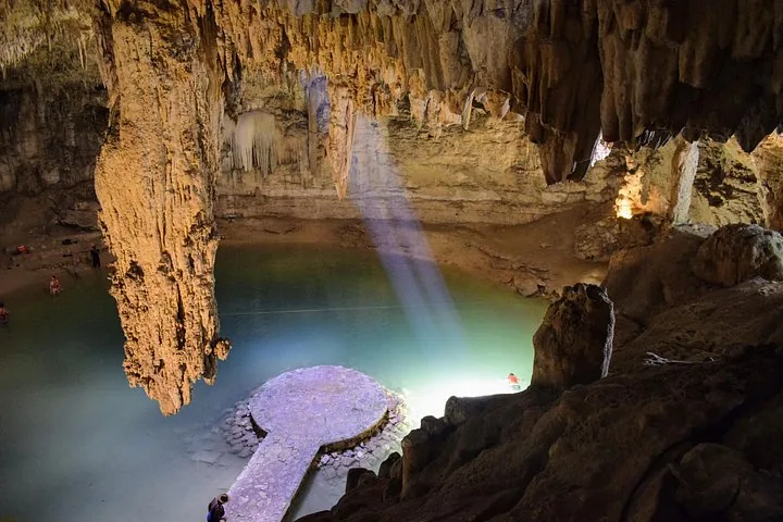 Un rayon de soleil illumine la plateforme en pierre et le bassin à l'intérieur du Cenote Suytun.