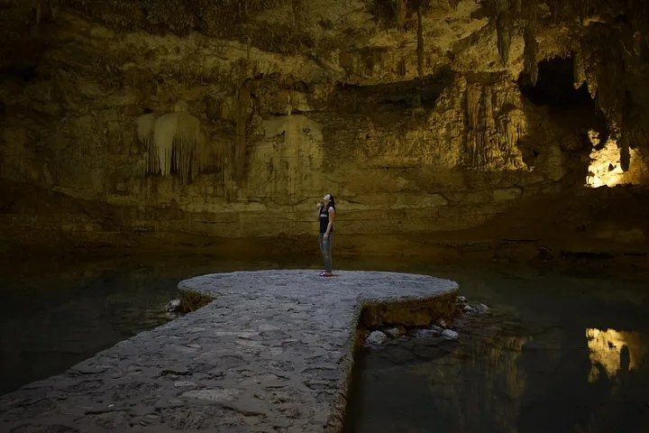 A person stands on the circular stone platform in a dimly lit cenote.