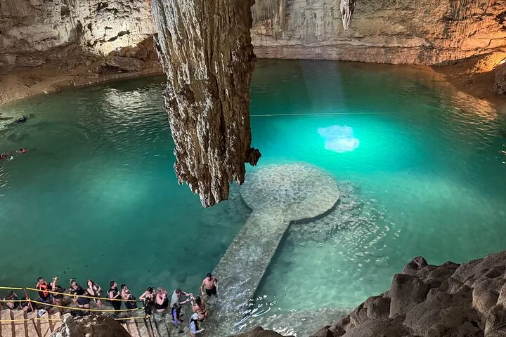 Tourists gather around the edge of Cenote Suytun near a large stalactite.